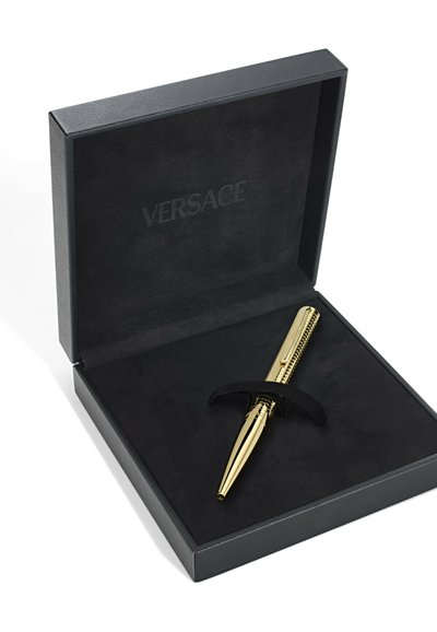 Złoty długopis z teksturowanym korpusem, umieszczony w czarnej aksamitnej pudełku z dopasowanym uchwytem, z logo "VERSACE" na wewnętrznej pokrywie.