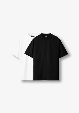 Dve enostavni bombažni majici z kratkimi rokavi, ena črna spredaj in delno vidna bela za njo, prikazani na belem ozadju.