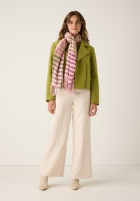 Grüne kurze Jacke, rosa-weißer karierter Schal, beige weite Hose und beige Ankle Boots. Glatte Texturen überall.