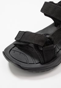 Black sandals featuring adjustable fabric straps, textured footbed, and a durable rubber sole with a patterned tread for grip.