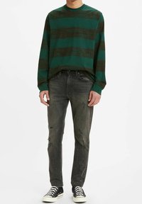 Camisa de manga larga a rayas verdes y negras combinada con jeans oscuros desgastados y zapatillas negras. Material de algodón, corte relajado, crea un look informal.