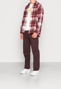 Rød og hvid ternet skjorte, hvid grafisk t-shirt, bordeaux bukser og hvide sneakers. Afslappet pasform, knap-ned krave, lange ærmer.