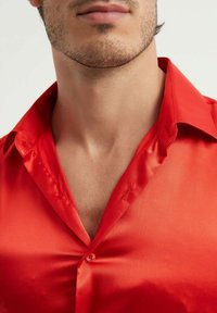 Chemise en satin rouge avec un col structuré, texture lisse et un petit bouton. Le tissu a une finition brillante qui met en valeur sa couleur vive.