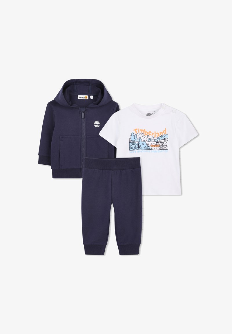 Donkerblauw zip-up hoodie en broek set met wit T-shirt met korte mouwen met een kleurrijke afbeelding van kamperen in de buitenlucht en het Timberland-logo.