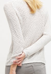 Jasnobeżowy sweter dziany z fakturowanym wzorem, długimi rękawami i dopasowanym krojem, z ściągaczami przy brzegu i mankietach.