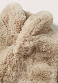 Tessuto in pelliccia finta di un morbido colore beige, caratterizzato da una texture pelosa con altezze del pelo variabili e un aspetto soffice.