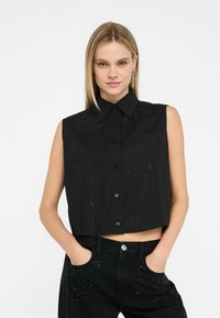 Cămașă scurtă, fără mâneci, de culoare neagră, cu închidere prin buton, dintr-un material texturat cu modele verticale și un singur buzunar pe piept.