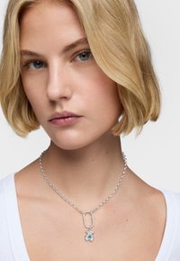 Srebrny łańcuszek z centralnym wisiorkiem z niebieskimi akcentami. Minimalistyczny design, gładka tekstura i regulowana długość.