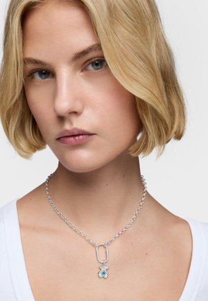 Silberkette mit einem zentralen Anhänger und blauen Akzenten. Minimalistisches Design mit glatter Textur und verstellbarer Länge.