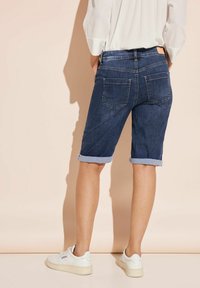 Shorts de mezclilla con dobladillo enrollado, color azul oscuro, que cuentan con dos bolsillos traseros y una cintura lisa. Combinados con zapatillas blancas.