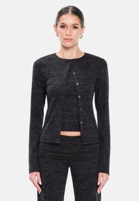 Cardigan nera a maglia con scollatura rotonda, maniche lunghe e bottoni frontali. Indossato sopra un top abbinato, realizzato in tessuto morbido e testurizzato.