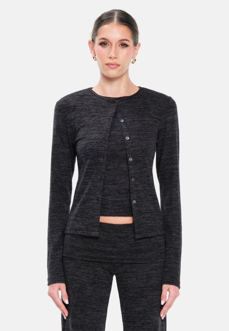 Svart stickad cardigan med rund halsringning, långa ärmar och knappar fram. Bärs över en matchande topp, tillverkad av mjukt strukturerat tyg.