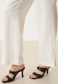 Vita linnebyxor med vida ben, med en ren design och slät textur, tillsammans med svarta sandaler med remmar och hög klack med spetsig tå.