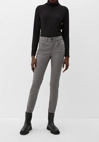 Šedé slim-fit kalhoty s hladkým povrchem, předními kapsami a knoflíkovým zapínáním. V kombinaci s černým rolákem s dlouhým rukávem a černými botami.