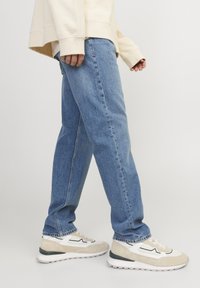 Svijetloplave traperice opuštenog kroja s blagim izblijedjelostima, uparene s bež i bijelim tenisicama s crnom akcentnom linijom.