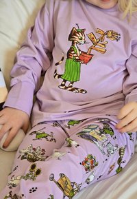 Lila långärmad skjorta med en katt som håller en kruka, tillsammans med mönstrade lavendelfärgade pyjamasbyxor med olika bondgårdsdjur och objekt.