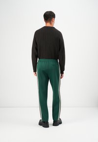 Pulover negru cu nervuri și pantaloni de trening verzi cu dungi albe pe lateral, având un elastic în talie, asortați cu pantofi negri masivi.