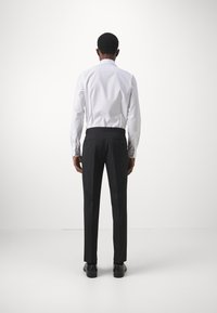 Hvid langærmet skjorte og sorte bukser. Skjorten har krave; bukserne har baglommer og en skræddersyet pasform. Sorte sko fuldender outfittet.