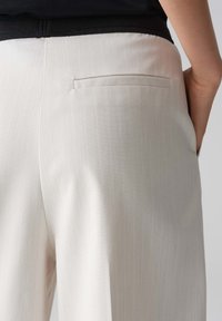 Pantaloni su misura a righe di colore chiaro, con una tasca posteriore senza cuciture, realizzati in un tessuto liscio. Presentano una leggera lucentezza e un taglio classico.