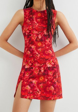 Ärmelloses rotes Kleid mit Blumenmuster und Seitenschlitz, getragen von einer Person mit langen dunklen Dreadlocks, Arme hinter dem Rücken angewinkelt.