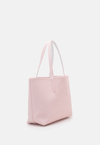 Sac fourre-tout rose avec deux longues anses, texture lisse, forme structurée et détail subtil du logo. Matériau solide pour un usage quotidien.