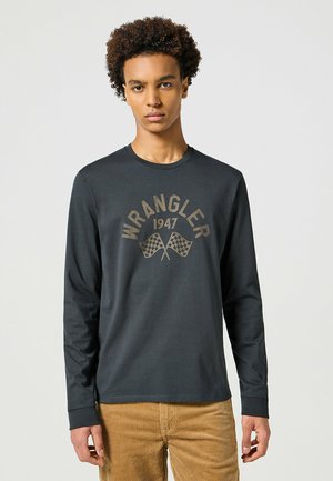Long-sleeve, dark gray cotton t-shirt featuring a gold Wrangler logo and checkered flags. Smooth texture, classic crew neck design.