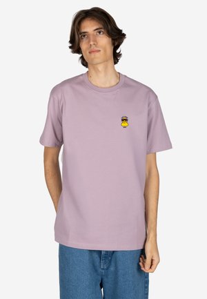 Young man wearing a light purple t-shirt with a small yellow duck graphic on the chest, paired with blue jeans against a white background.