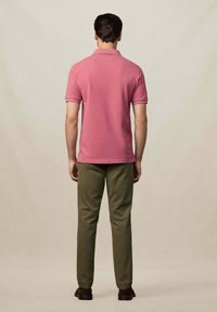Ružová polo košeľa vyrobená z bavlny, s krátkymi rukávmi. V kombinácii s olivovými nohavicami, rovného strihu a tmavohnedými topánkami, zobrazené zozadu.