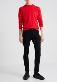 Röd långärmad skjorta i slätt tyg, kombinerad med slim fit svarta jeans och svarta sneakers. Har en liten logotyp på skjortan.