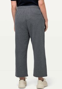 Pantalones grises de pierna ancha, texturizados, con cintura elastizada y un bolsillo trasero, combinados con zapatillas beige.