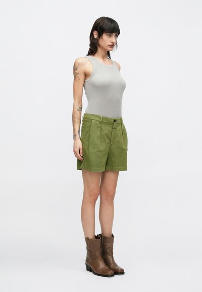 Γκρι ριμπ τοπ χωρίς μανίκια συνδυασμένο με πράσινα σορτς ψηλόμεσα. Τα σορτς έχουν πιέτες μπροστά και συνοδεύονται από καφέ μποτάκια μέχρι τον αστράγαλο.