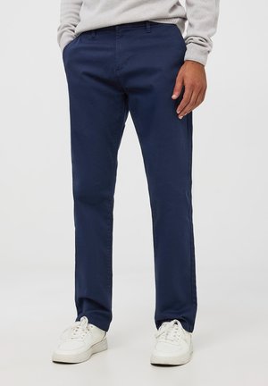 Chino in cotone blu navy con design a gamba dritta, dotato di tasche laterali e texture liscia, abbinati a sneakers bianche.