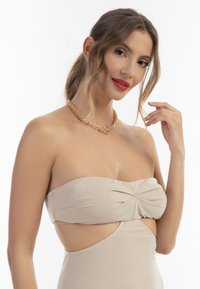 Abito nudo senza spalline con fianchi intagliati, caratterizzato da un corpetto attorcigliato. Una collana di catena dorata aggiunge dettagli. Texture liscia e aderente.