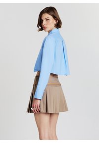 Camicia corta blu chiaro con colletto e piega sul retro. Abbinata a una gonna beige a pieghe e una cintura sottile color sabbia.