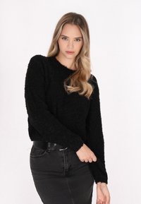 Schwarzer, flauschiger Pullover mit Rundhalsausschnitt und langen Ärmeln, kombiniert mit einem hoch taillierten, schwarzen Jeansrock aus strukturiertem Stoff, ohne sichtbare Muster.