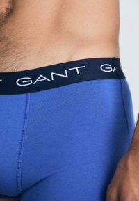 Kék pamut boxer alsónadrág sötétkék elasztikus derékkal, amelyen fehér "GANT" felirat található, sima textúrával és testhezálló fazonnal.