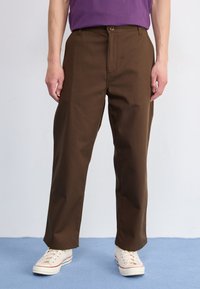 Bruine katoenen broek met een recht gesneden ontwerp, voorzien van een sluiting met een knoop aan de voorkant en zijzakken, gecombineerd met beige sneakers.