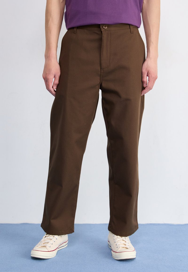 Bruine katoenen broek met een recht gesneden ontwerp, voorzien van een sluiting met een knoop aan de voorkant en zijzakken, gecombineerd met beige sneakers.