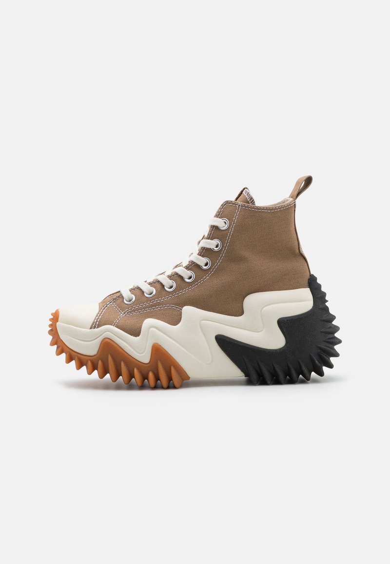 Brown canvas high-top sneakers with white laces, prominent zigzag sole in cream and black, featuring a textured rubber outsole and pull tab.