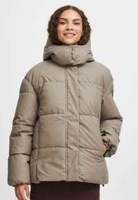 Beige pufferjakke med høj krave, quiltet design og elastiske manchetter. Har sidelommer og en løs pasform for komfort.