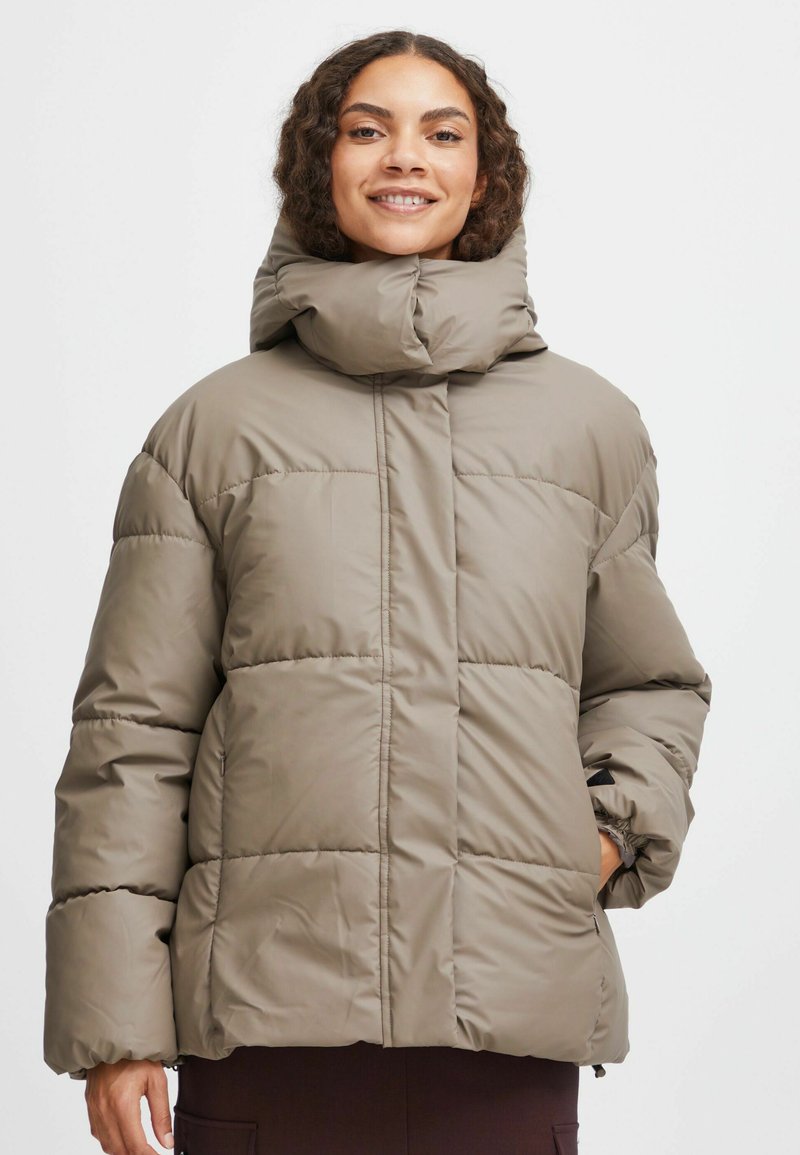 Beige Kapuzenjacke mit hohem Kragen, gestepptem Design und elastischen Bündchen. Mit seitlichen Taschen und einem lockeren Schnitt für zusätzlichen Komfort.