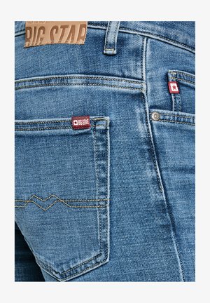 Sinised teksapüksid, mille tagataskutel on punased Big Star kaubamärgi sildid ja nahast Big Star silt vöökohal.