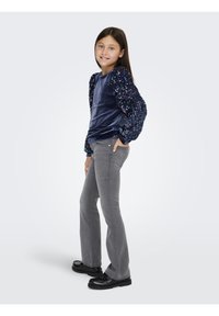 Top de veludo azul-marinho com mangas bufantes de lantejoulas, combinado com jeans cinzentos flare e sapatos pretos robustos. Textura suave e detalhes brilhantes.
