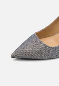 Spidse sko til kvinder med sølvglitrende overflade og beige læderinteriør på hvid baggrund.