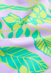 Violets audums ar spilgti zaļu un dzeltenu tropisko lapu un ziedu rakstu, attēlota tuvplānā ar redzamām krokām un faktūru.