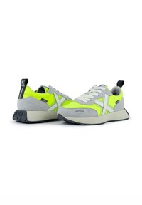 Chaussures de sport avec une tige en suede gris et mesh jaune néon, accents blancs et une semelle extérieure en caoutchouc noir avec un languette de tirage marquée.