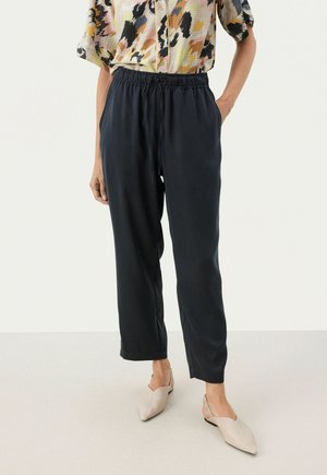 Black, loose-fitting, elastic-waist pants with a smooth texture. Paired with a colorful patterned shirt and light-colored shoes.