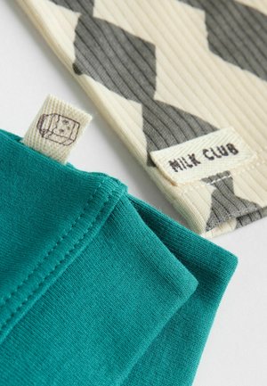 Blåt bomuldsstof med synlige syninger ved siden af et mønstret beige og gråt tekstil. Etiketter viser "MILK CLUB" og en grafik.