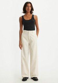 Witte wijde broeken gecombineerd met een zwart geribd tanktop. De stof is soepel, met een losse pasvorm en een hoge taille. Zwarte schoenen maken de look compleet.