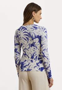 Knitted sweater featuring a white base with blue floral patterns. Long sleeves and ribbed texture, styled with a round neckline.